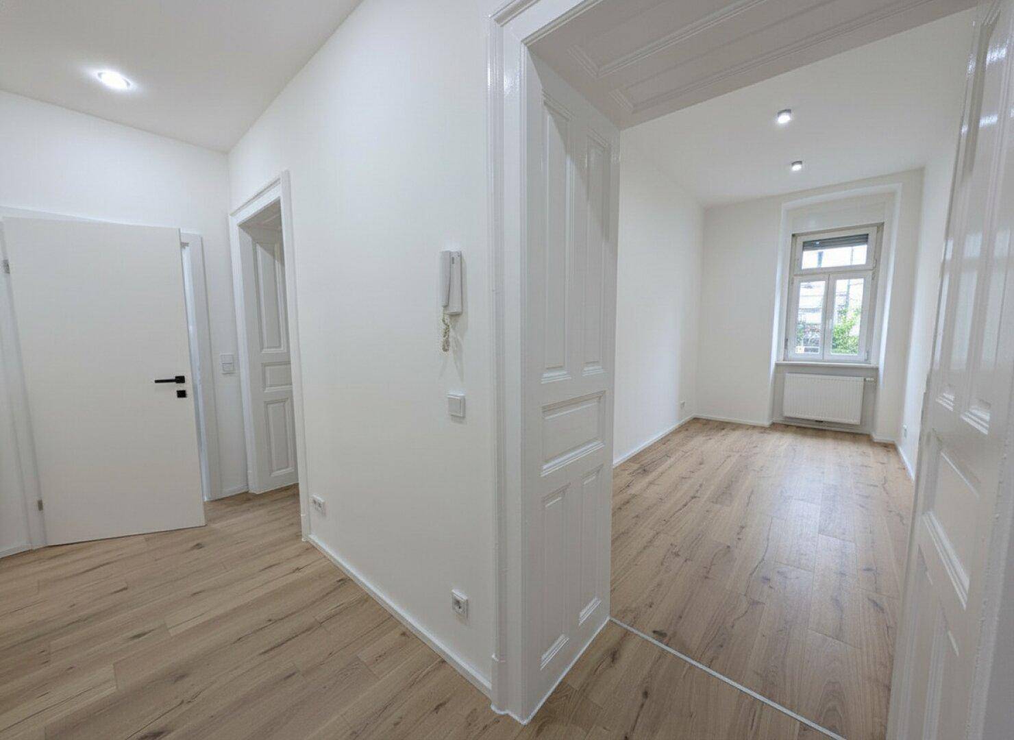 Heller Flur mit Holzboden, der den Blick in einen angrenzenden Raum mit Fenster freigibt.