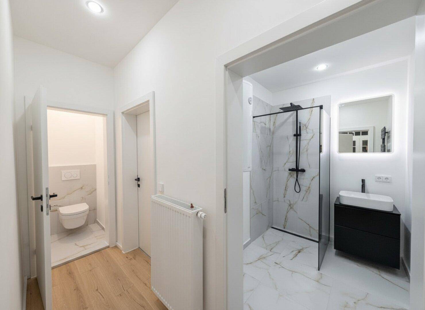 Moderner Flur mit Zugang zu einem stilvollen Badezimmer mit begehbarer Dusche und separatem WC.