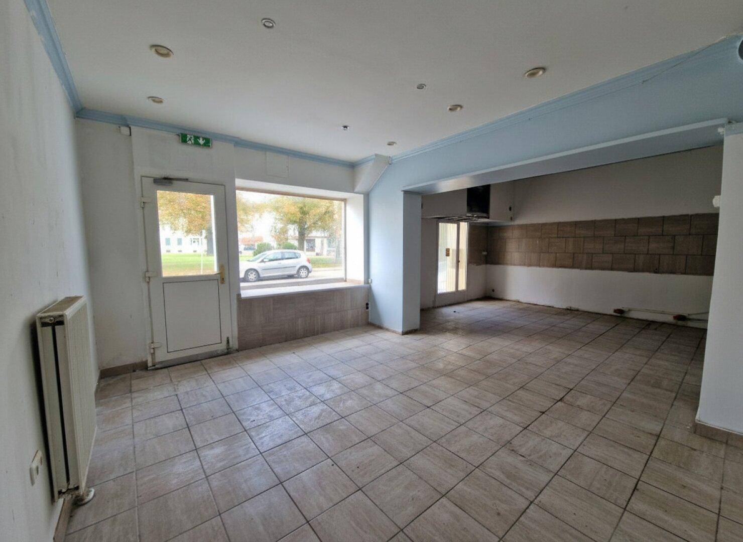 Leerer Gewerberaum mit Fliesenboden, großen Fenstern zur Straße und einem Heizkörper an der Wand.