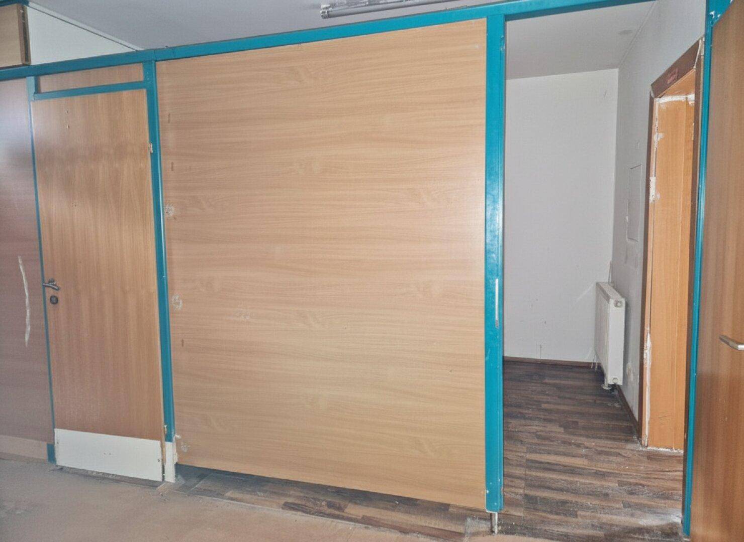 Innenraum mit Holzboden und einer verschiebbaren Holztrennwand, die den Raum unterteilt.