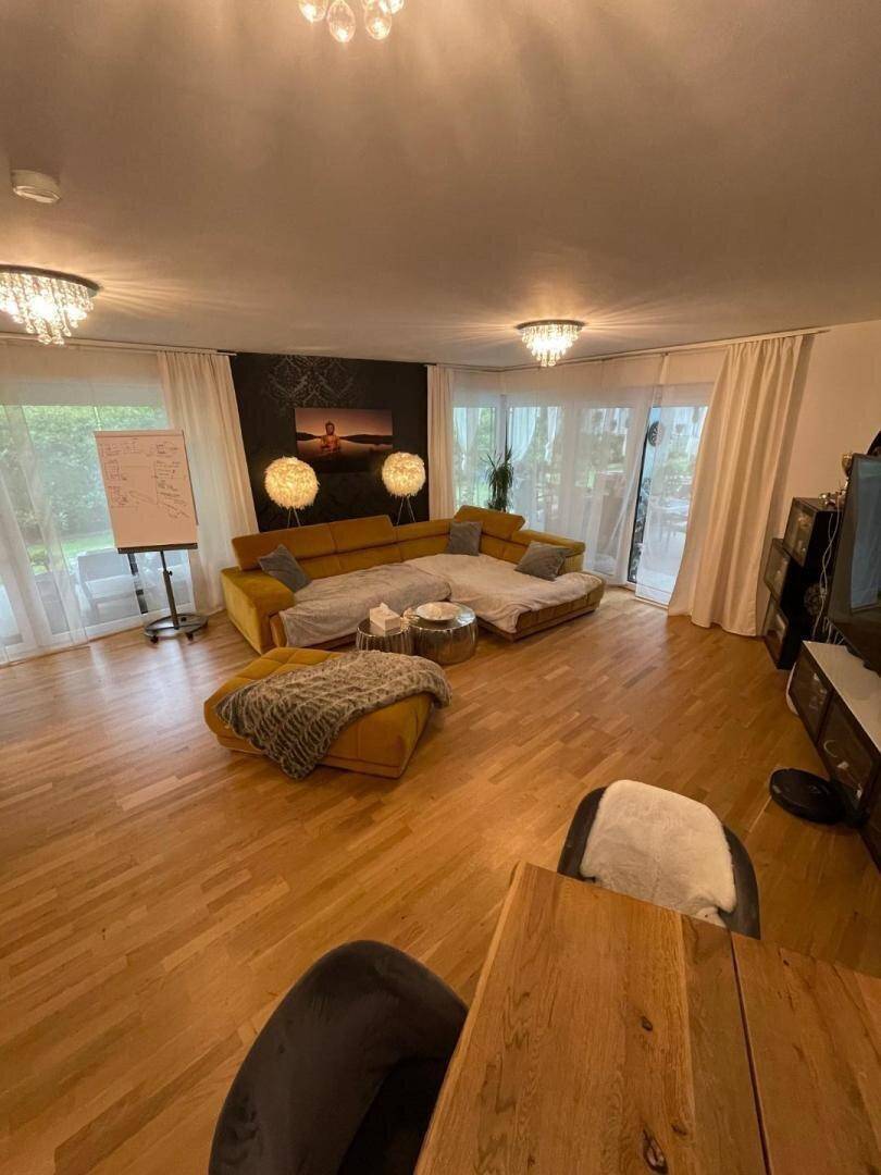 Gemütliches Wohnzimmer mit großem gelben Sofa, Holzboden und viel Tageslicht durch die Fenster.