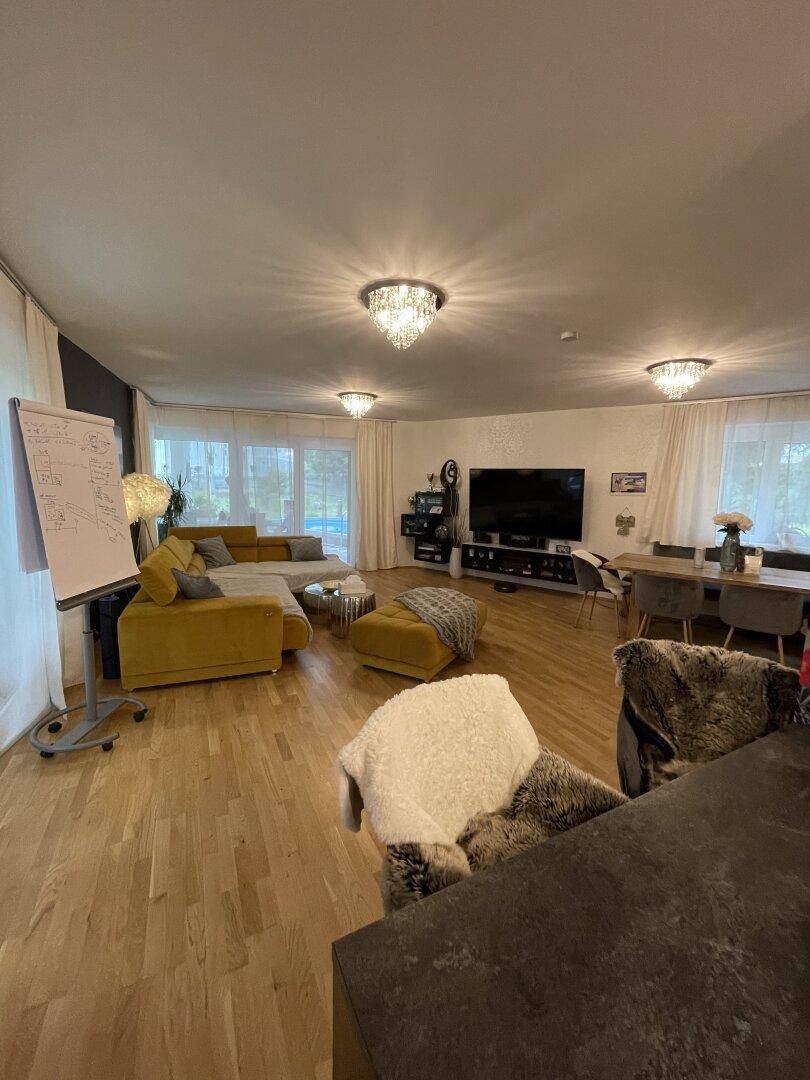 Weitläufiger Wohn-Essbereich mit Holzboden, großem Fernseher und moderner Einrichtung.