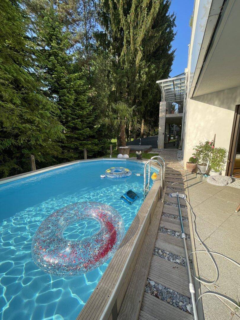 Detailansicht des Pools mit Holzumrandung und Kiesbereich, umgeben von viel Grün.