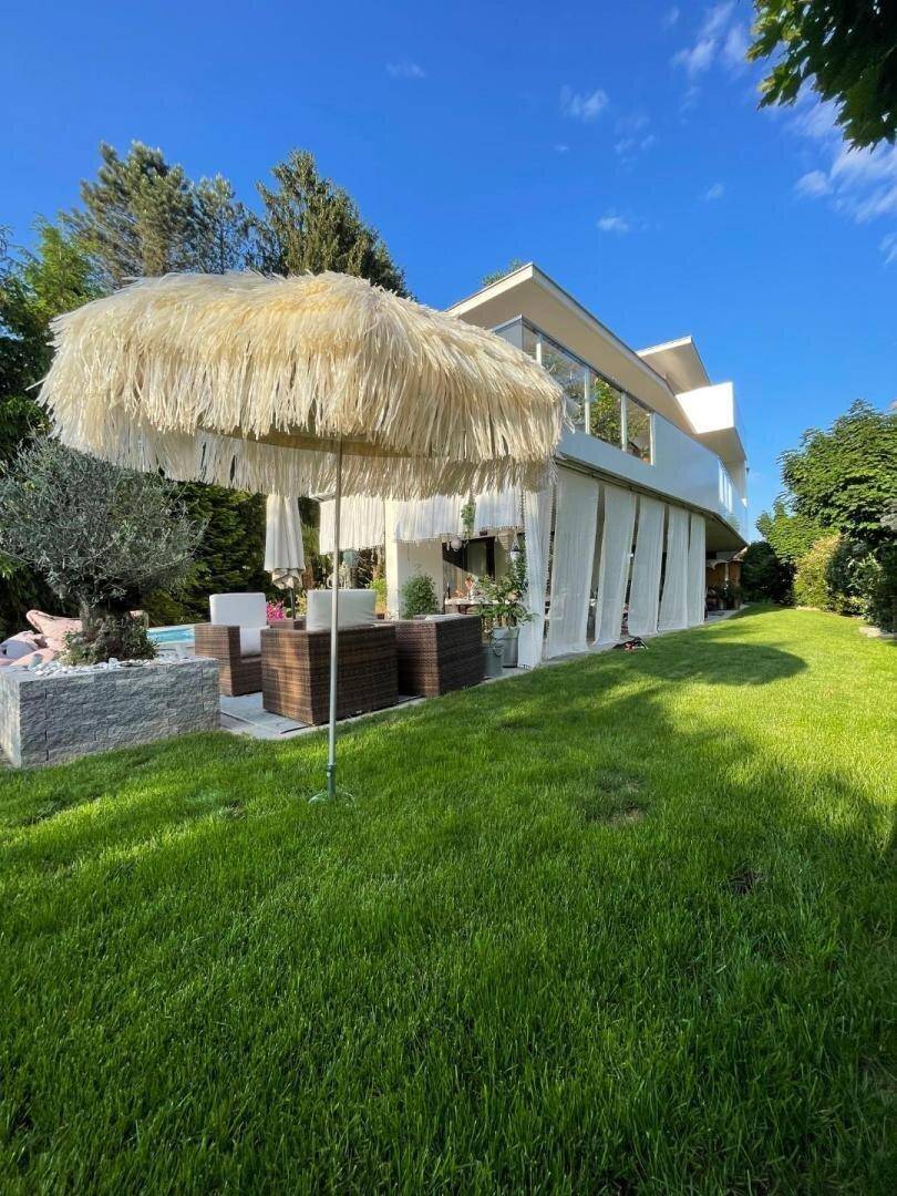 Weitläufiger Gartenbereich mit Rasen, großem Sonnenschirm und Blick auf das moderne Haus.