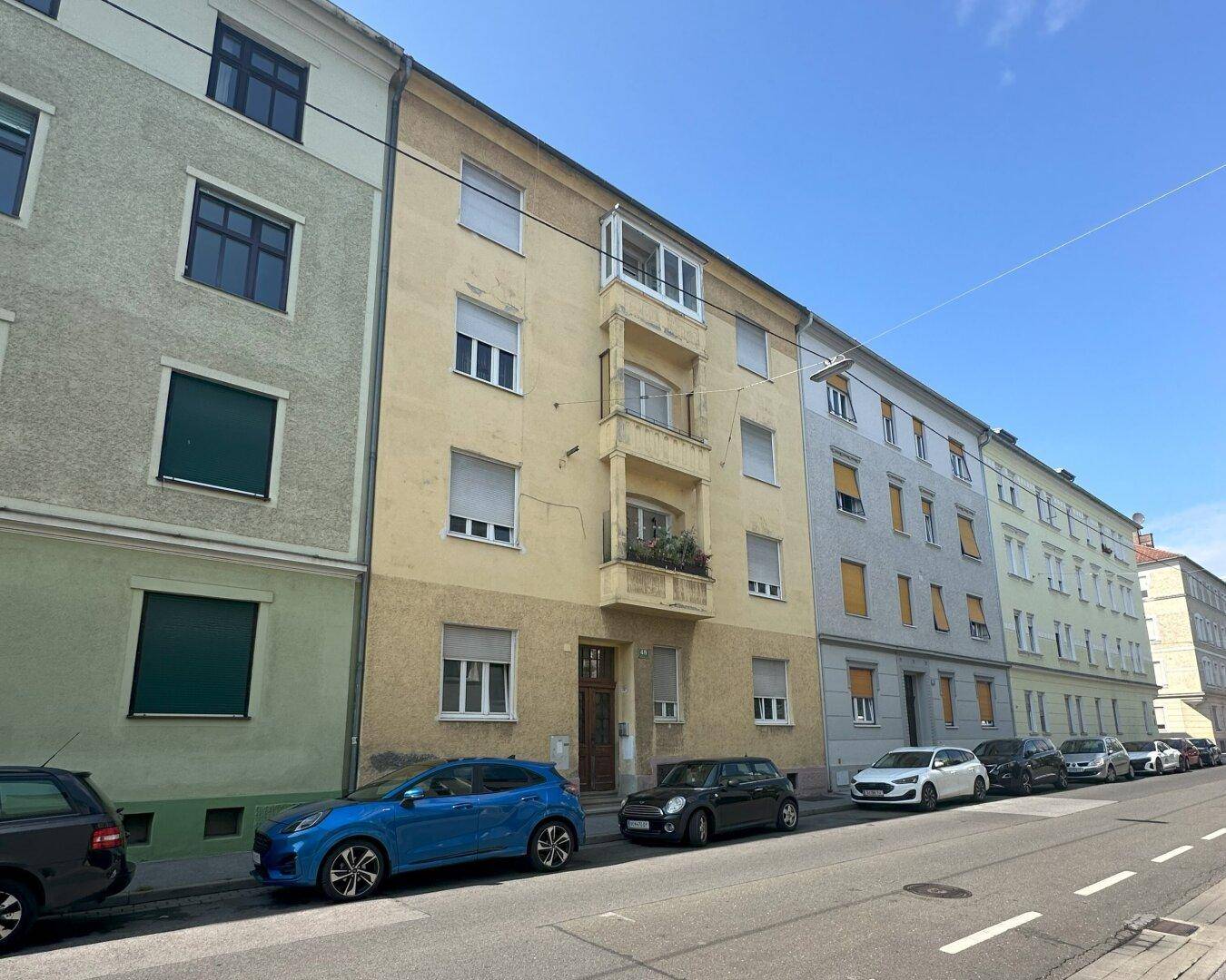 Fassade eines Mehrfamilienhauses an einer Straße mit parkenden Autos.