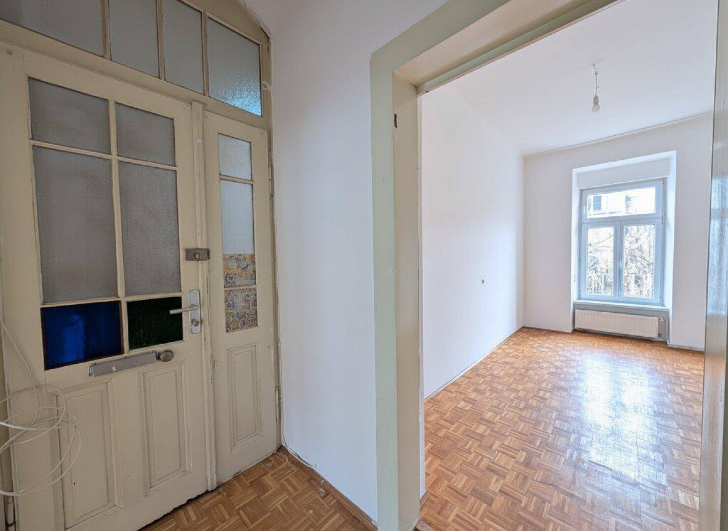 Eingangsbereich mit einer Holztür mit Glaseinsätzen und Blick in ein Zimmer mit Parkettboden.