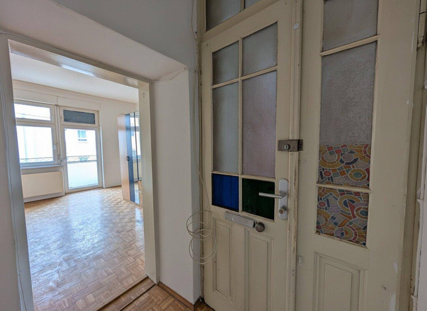 Eingangsbereich mit einer Holztür mit farbigen Glaseinsätzen und Blick in ein Zimmer.