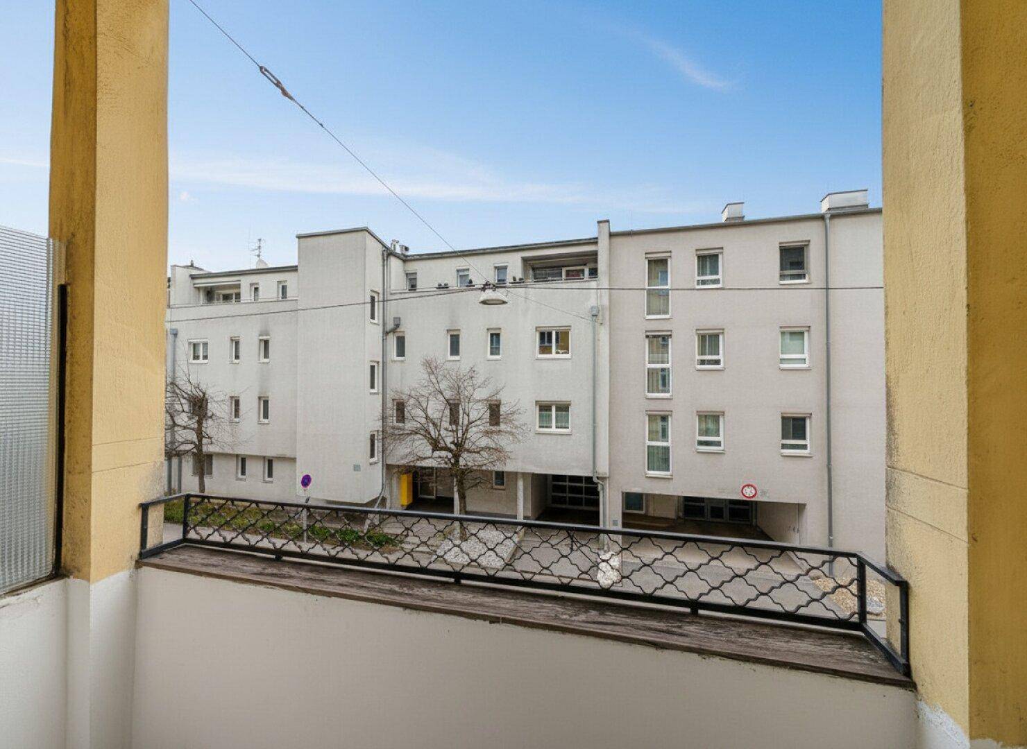 Balkon mit Blick auf einen Innenhof und ein gegenüberliegendes Gebäude.