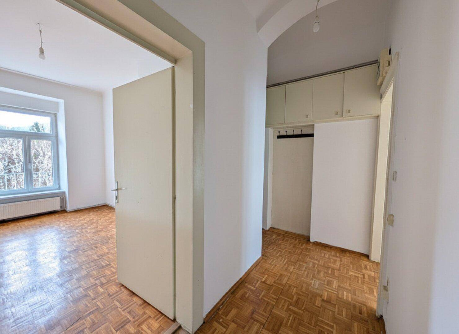 Flur mit Parkettboden und integrierten Wandschränken, der zu einem hellen Zimmer führt.