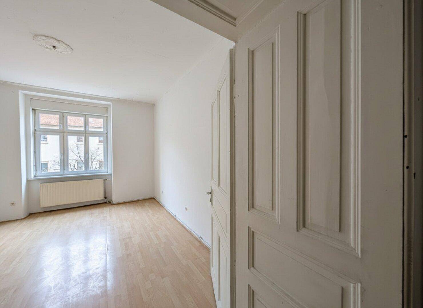 Heller, leerer Raum mit Laminatboden und einem Fenster mit Blick nach draußen.