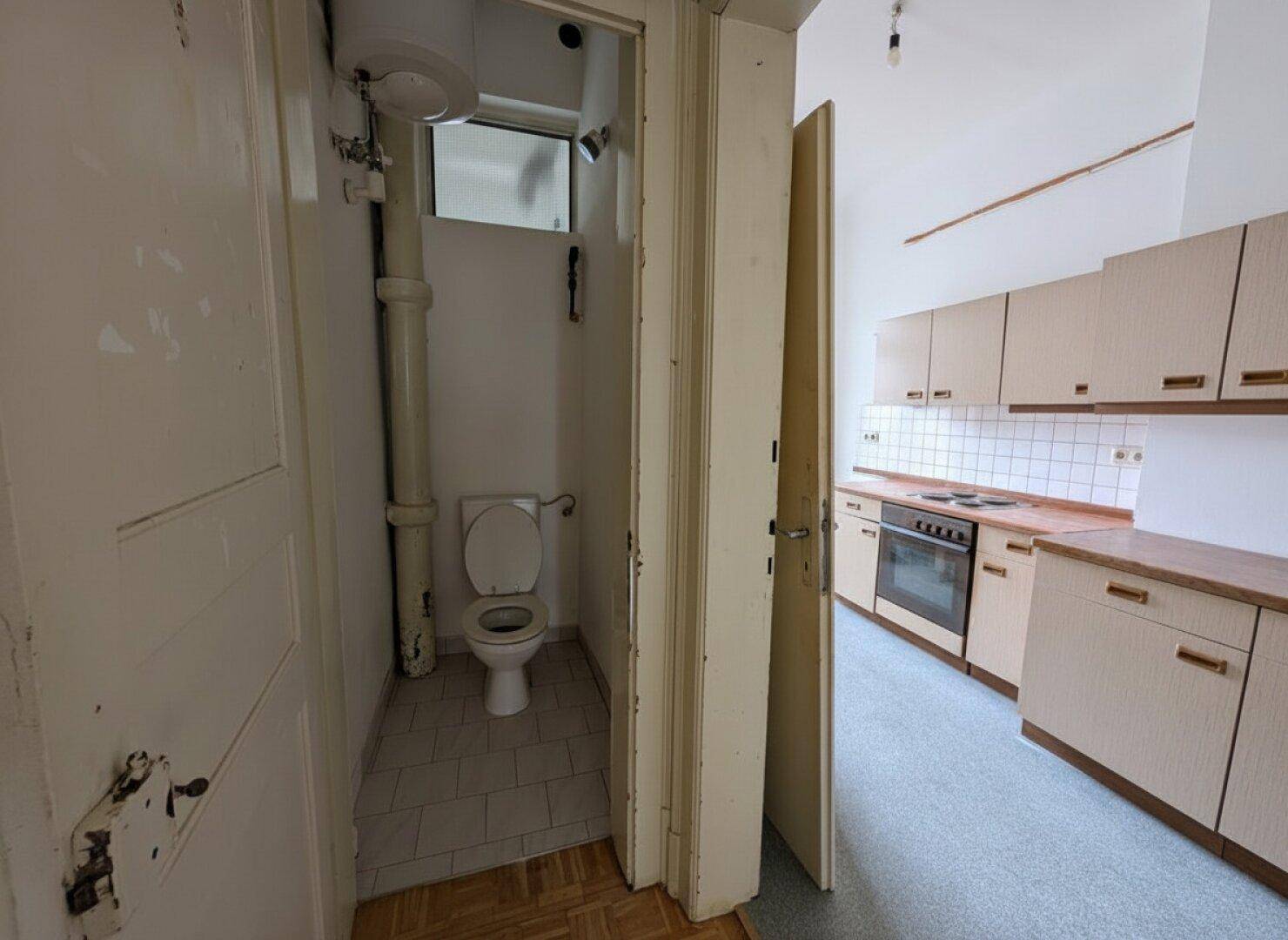Küche mit einfacher Einbauküche und Blick in eine separate Toilette.