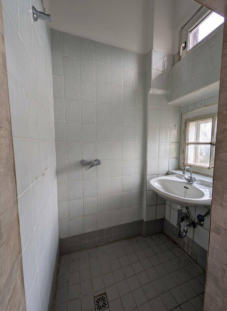Kleines Badezimmer mit Duschbereich, Waschbecken und Fenster.