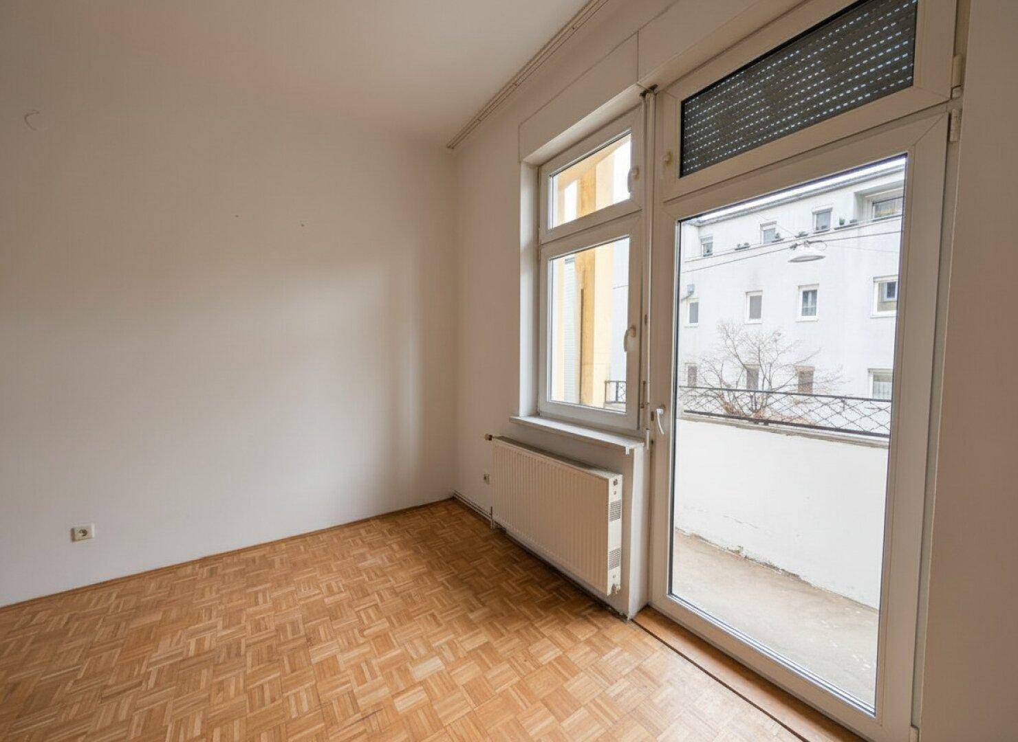Heller Raum mit Parkettboden und Zugang zu einem kleinen Balkon.