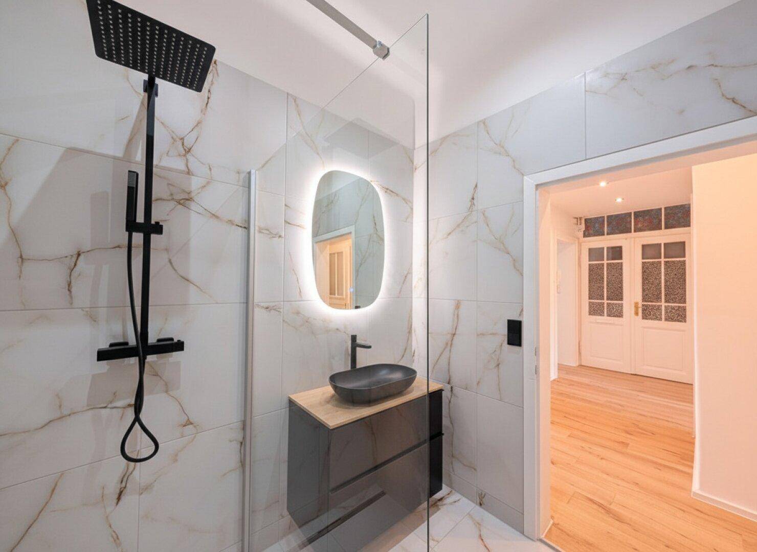 Stilvolles Badezimmer mit moderner Dusche, schwarzem Waschbecken und Blick in den Flur.