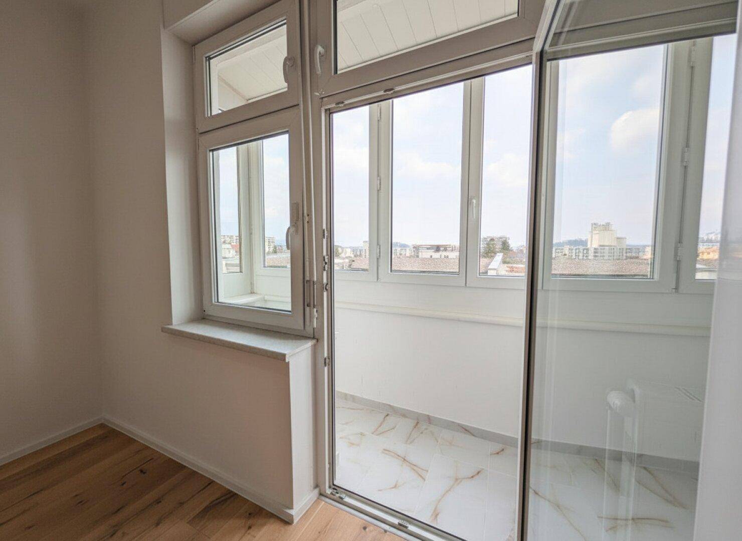 Heller, verglaster Balkon mit Fliesenboden und weitem Blick über die Stadt.