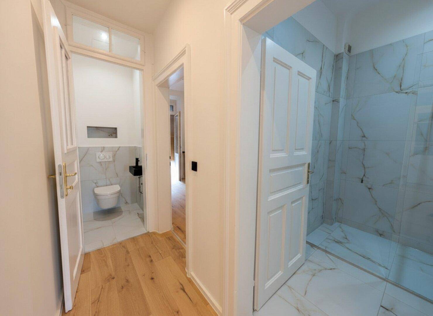 Heller Flur mit Holzfußboden, der zu einem Gäste-WC und einem modernen Badezimmer führt.