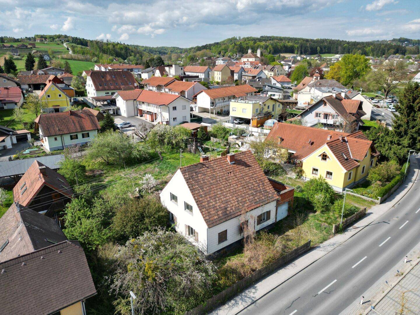 Luftaufnahme eines ländlichen Dorfes mit vielen Häusern und grüner Umgebung unter blauem Himmel.