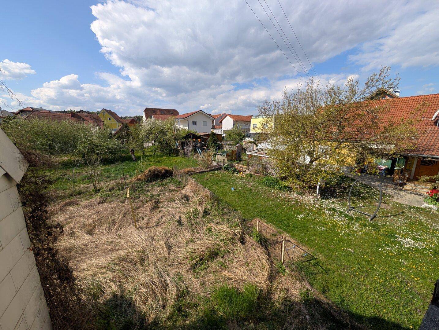 Weitblick von einer Terrasse über einen verwilderten Garten und die umliegende Wohnsiedlung.