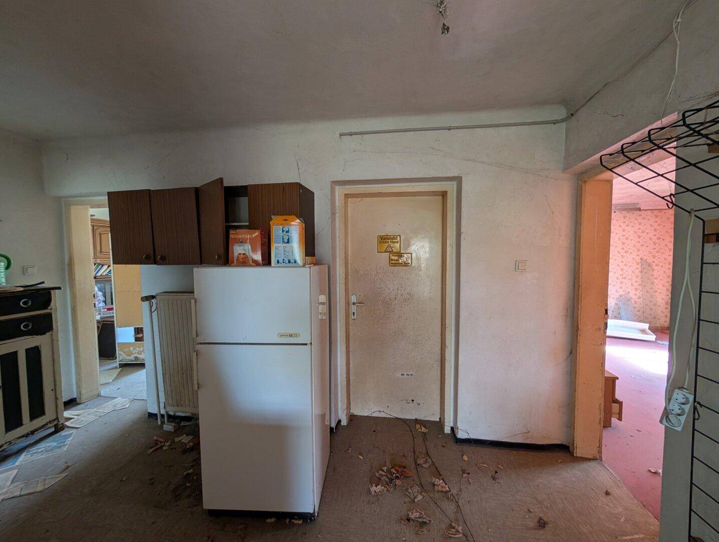 Unaufgeräumter Flur mit alter Einrichtung und einem Kühlschrank, der Renovierung benötigt.