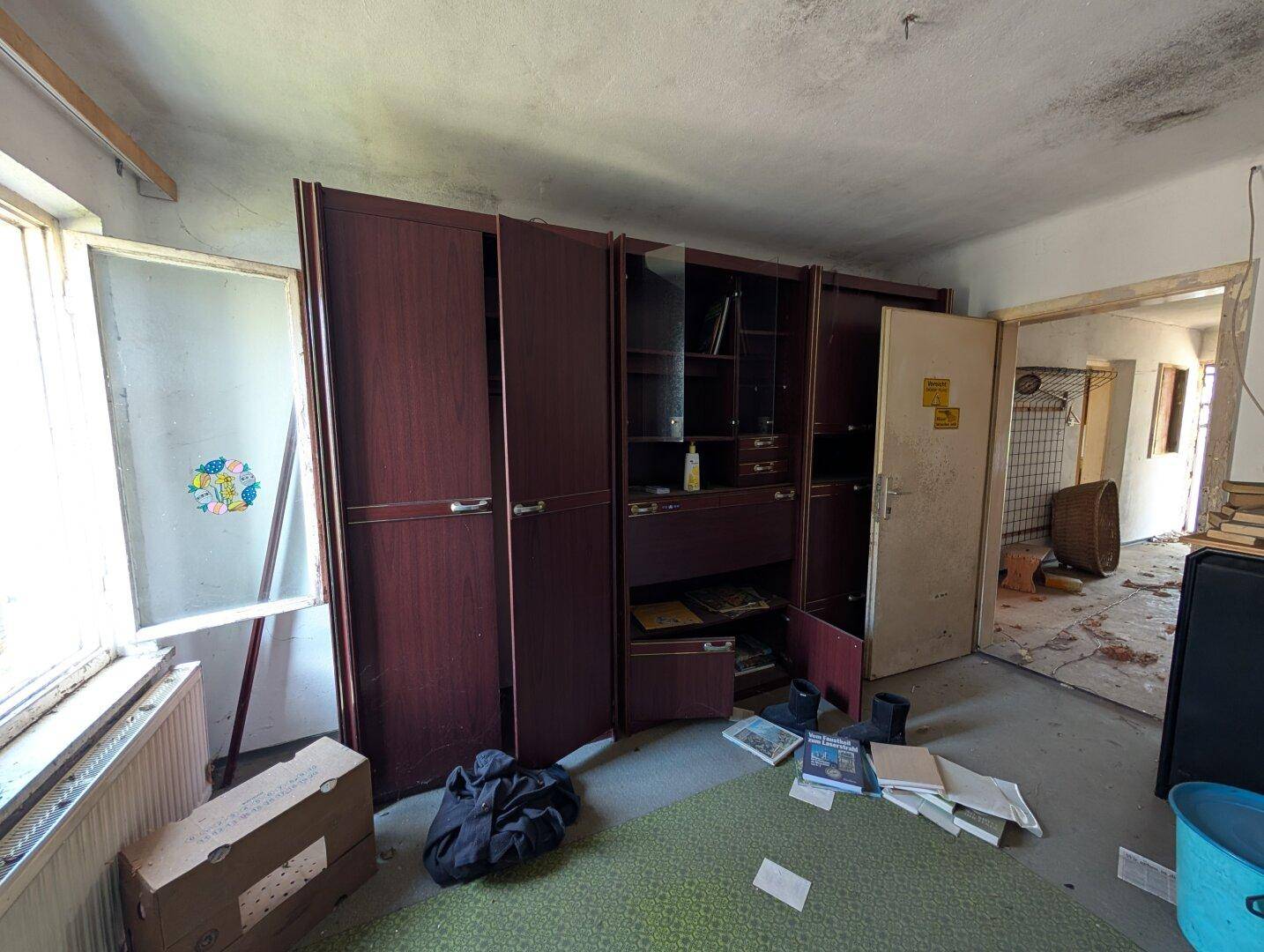 Zimmer mit großen Holzschränken und Blick in einen angrenzenden Flur, der Renovierung benötigt.