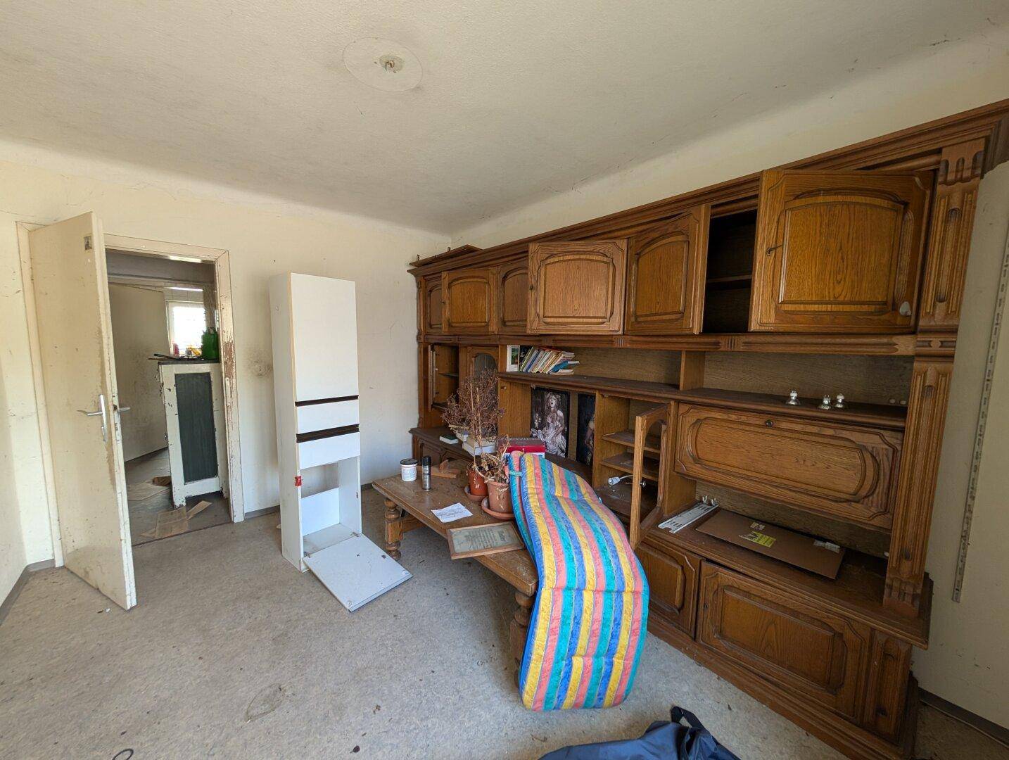 Zimmer mit großer, traditioneller Holzschrankwand und Blick in einen angrenzenden Raum.