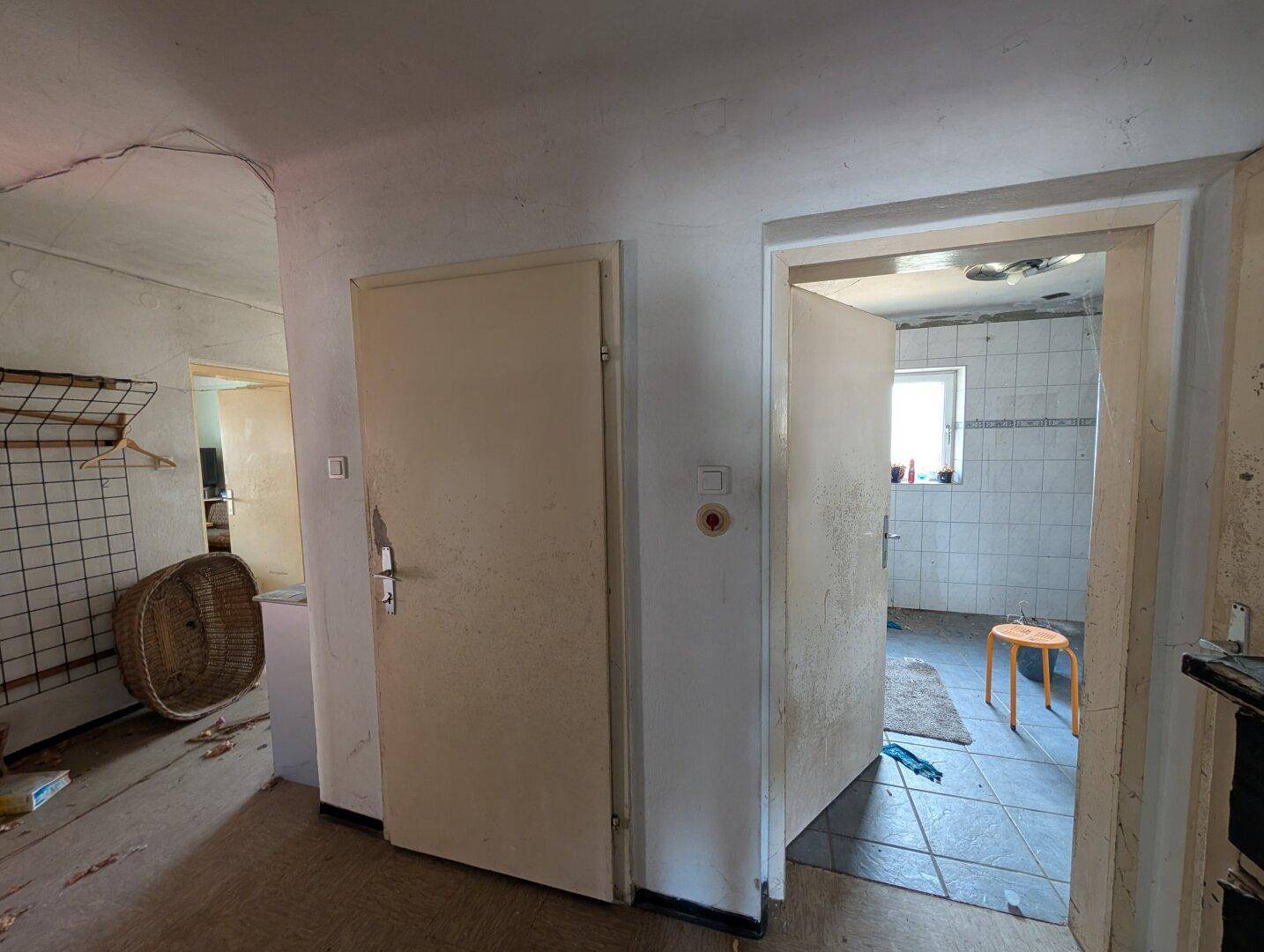Flur mit zwei Türen, eine davon führt in ein Badezimmer mit Fliesenboden.