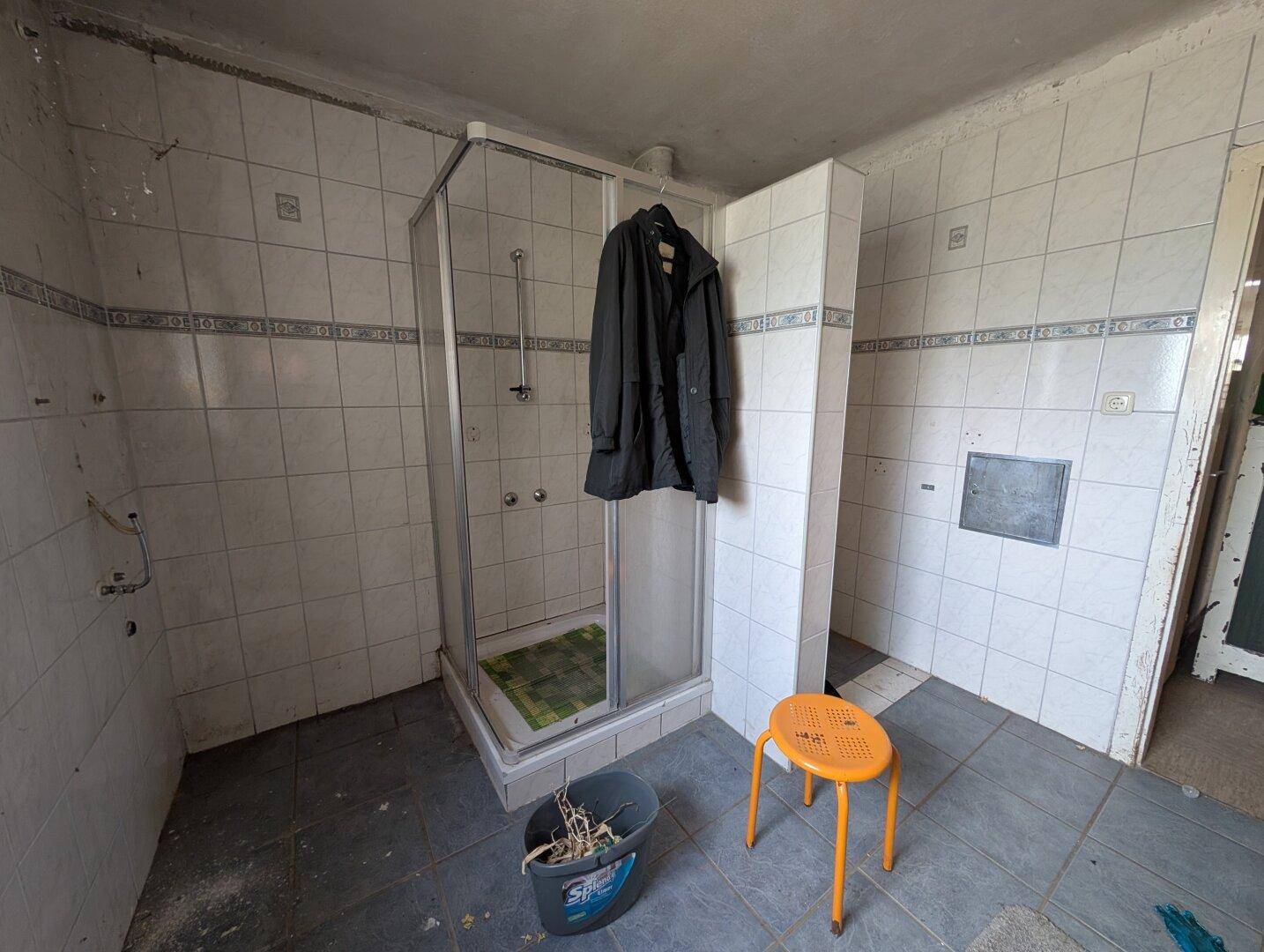 Badezimmer mit Duschkabine und hellen Fliesen, das eine umfassende Modernisierung benötigt.