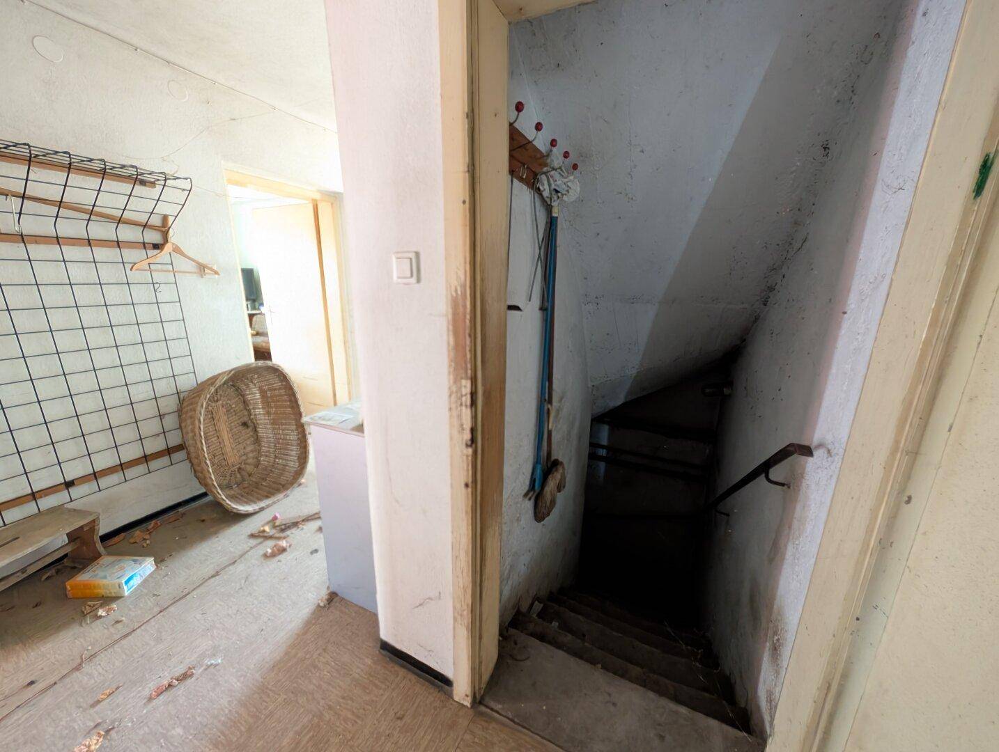 Flur mit Zugang zu einer dunklen Kellertreppe, die in das Untergeschoss führt.
