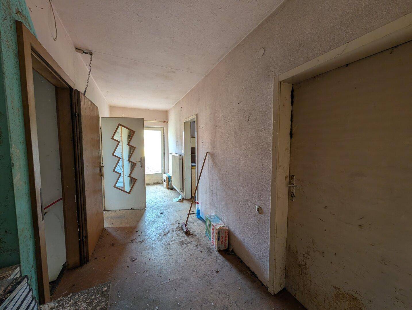 Langer Flur mit mehreren Türen und einem Fenster am Ende, der Renovierung benötigt.