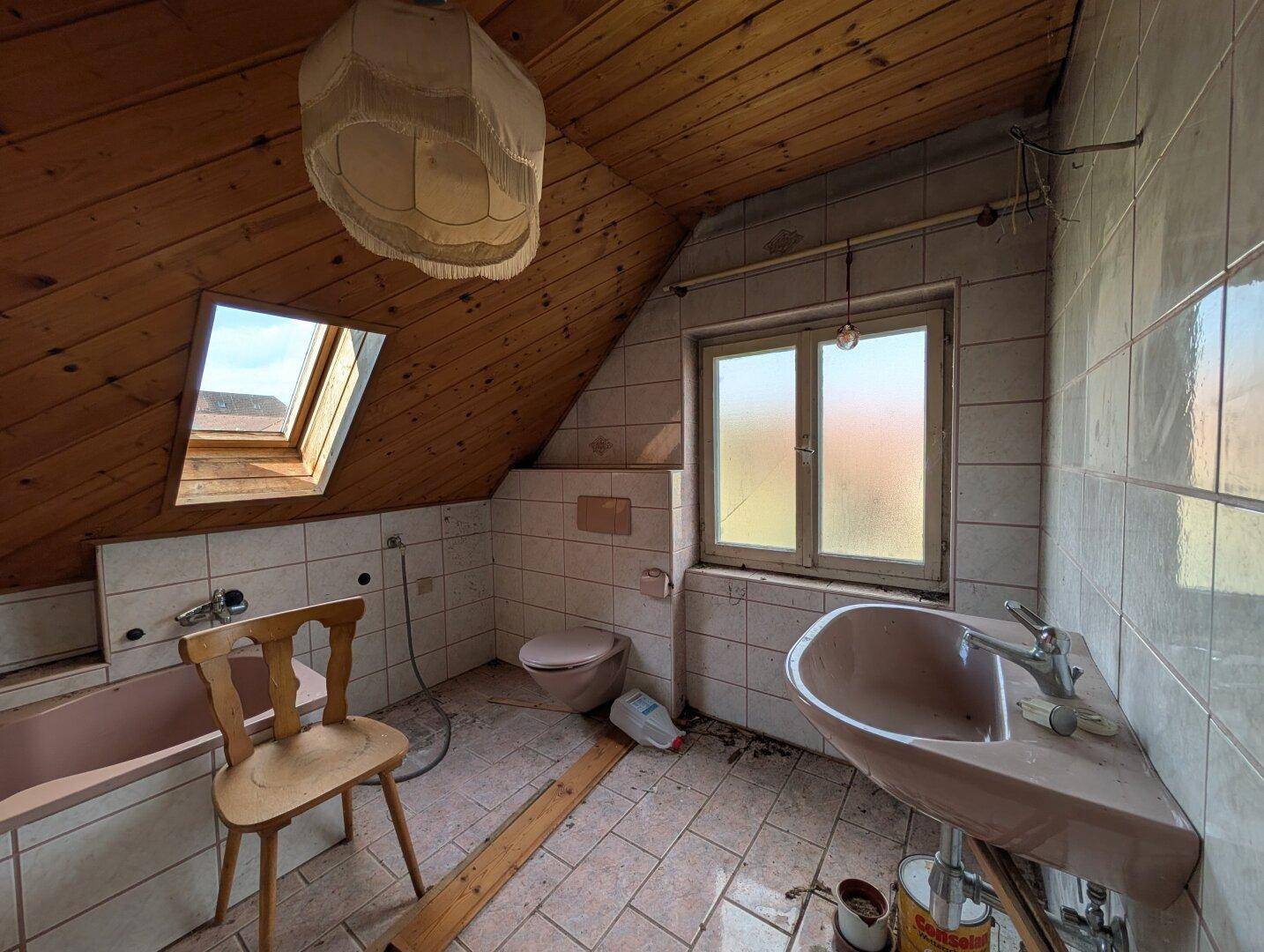 Badezimmer im Dachgeschoss mit Dachschräge, Dachfenster, Badewanne und Waschbecken in Pastellfarben.