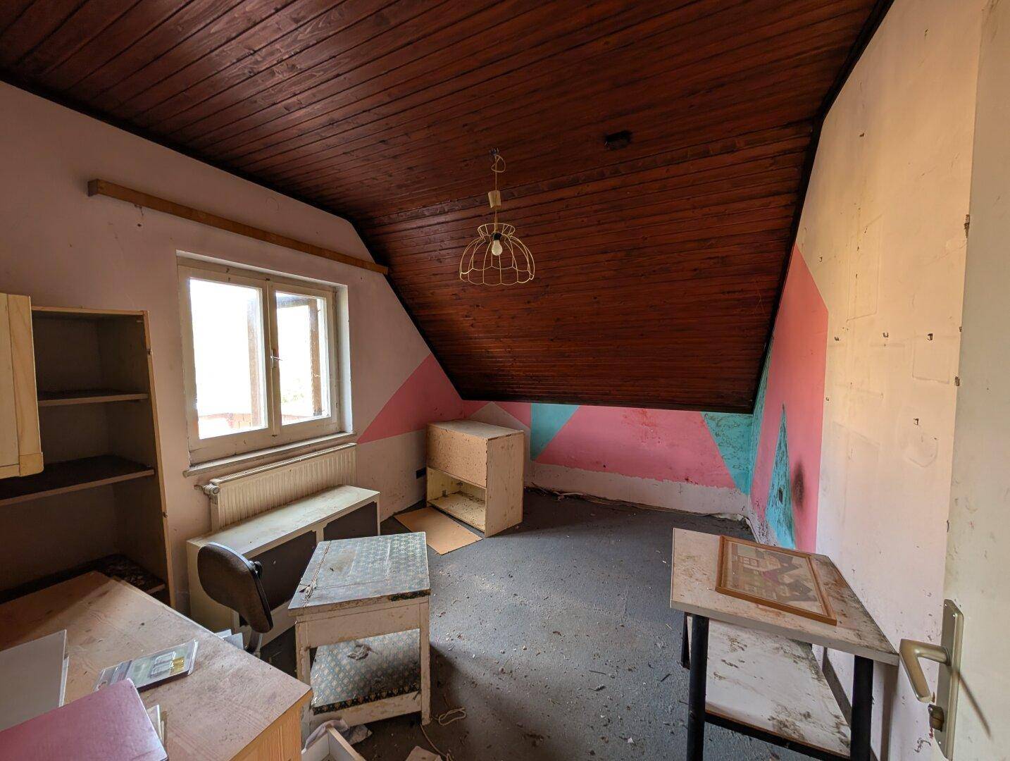 Dachzimmer mit Holzdecke, Dachschräge und bunten Wänden, das als Schlaf- oder Arbeitszimmer dienen könnte.