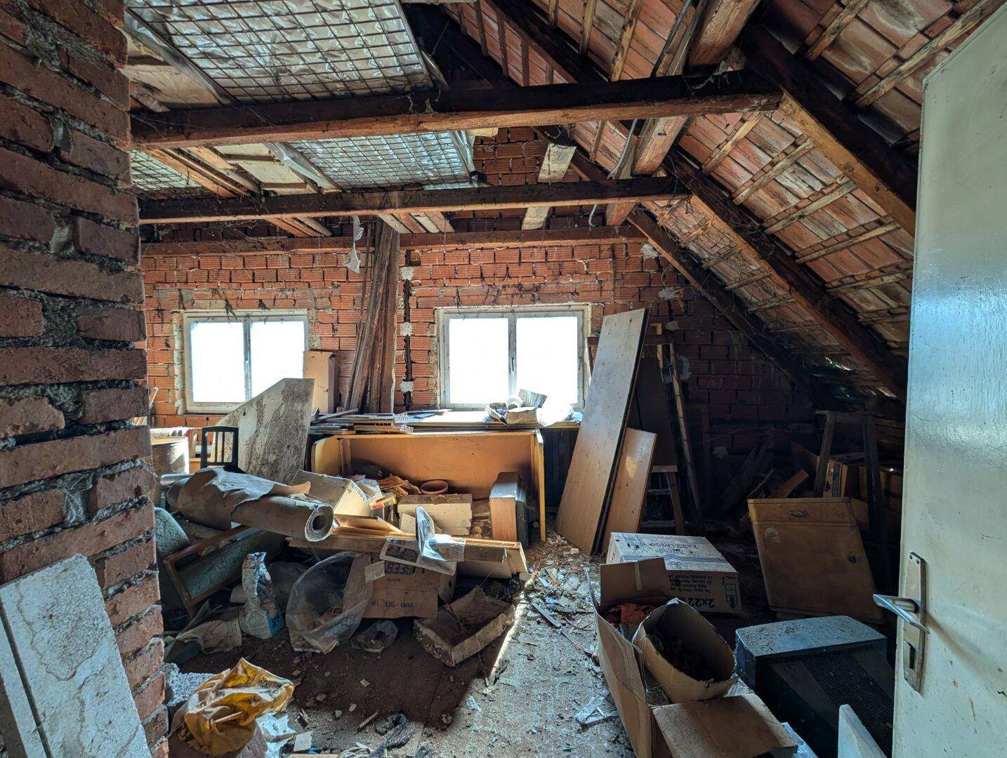 Dachboden im Rohbauzustand mit sichtbaren Holzbalken und Ziegelwänden, der viel Potenzial bietet.