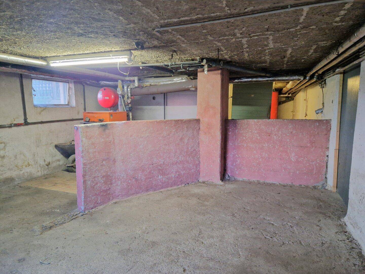 Unfertiger Kellerraum mit Betonboden und rosa gestrichenen Wänden, bietet Stauraum.