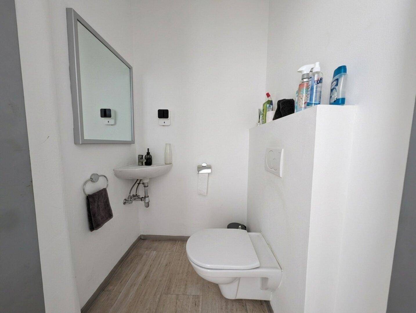 Helle Gästetoilette mit wandhängendem WC, kleinem Waschbecken und Spiegel, sauber und funktional.