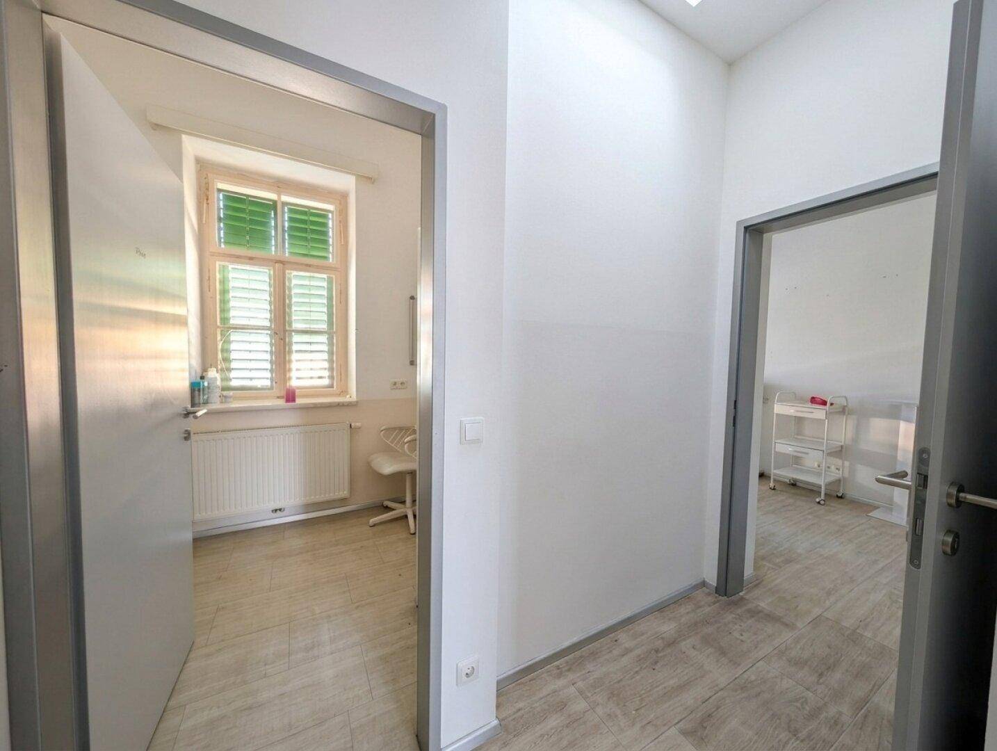 Heller Flur mit zwei offenen Türen, die zu weiteren Räumen mit Holzoptik-Boden und Tageslicht führen.