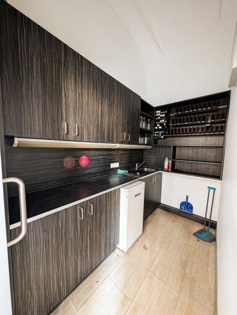 Funktionale Küchenzeile mit dunklen Holzschränken, Spüle und kleinem Kühlschrank, ideal für den Personalbereich.