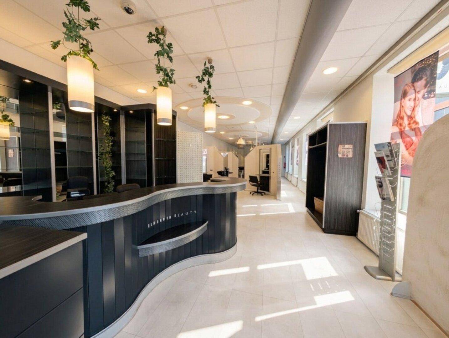 Langer Flur eines Salons mit Empfangstheke, Regalen und hellen Bodenfliesen, die den Raum optisch erweitern.