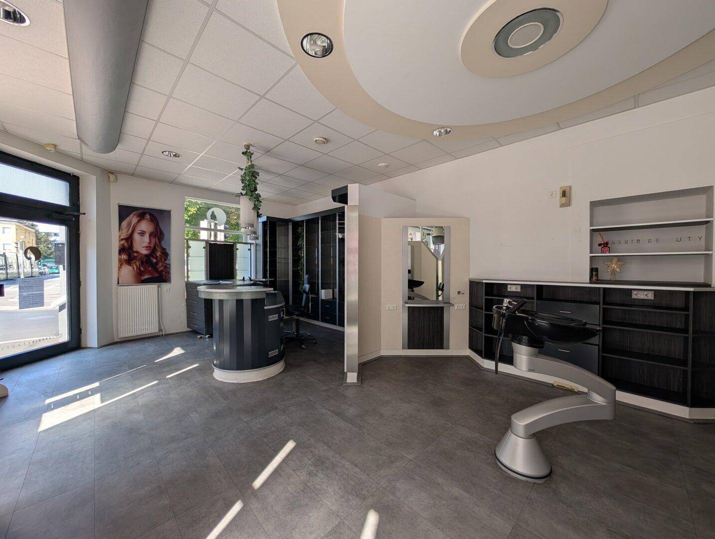 Empfangsbereich und Stylingplätze eines Salons mit dunklen Möbeln und hellen Böden, die eine moderne Atmosphäre schaffen.