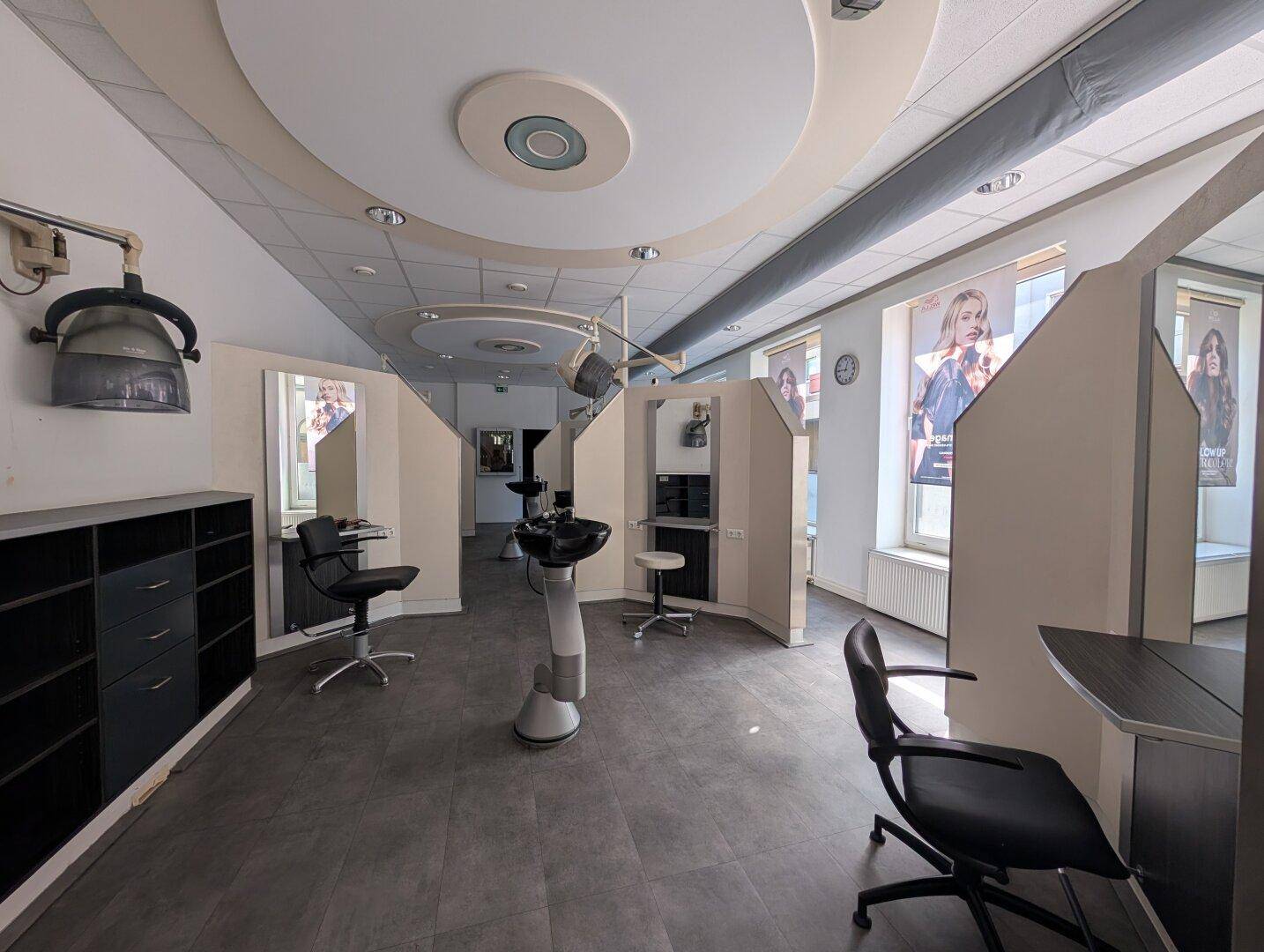 Stylingbereich eines Friseursalons mit mehreren Arbeitsplätzen, Trockenhauben und großen Fenstern für natürliches Licht.
