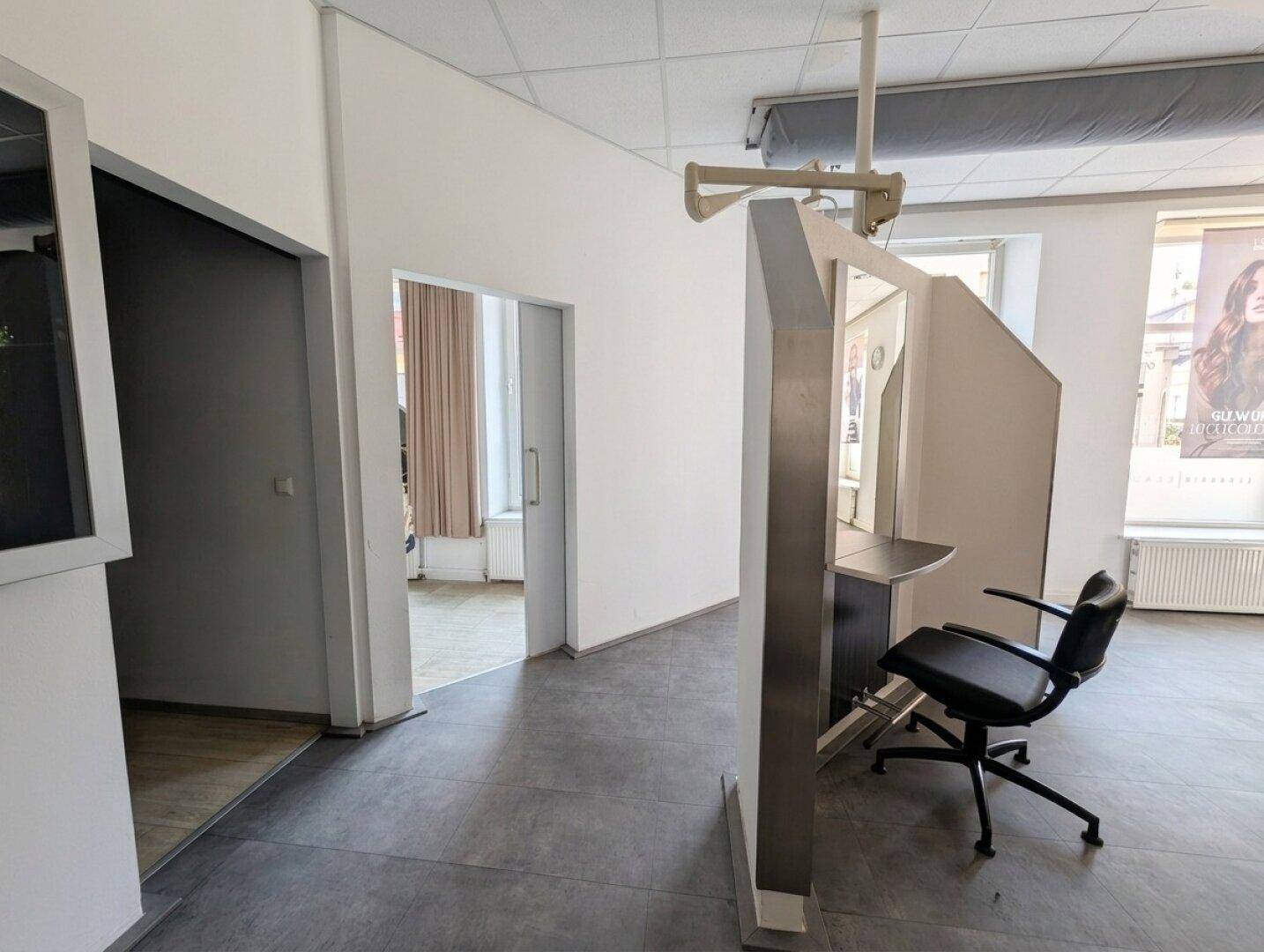Flur im Salon mit Blick auf einen Stylingplatz und eine offene Tür zu einem Nebenraum, alles in hellen Tönen.