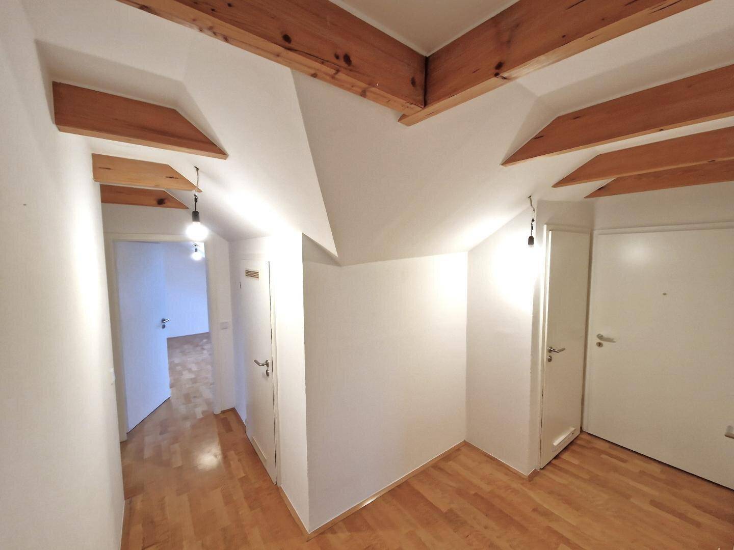 Leerer Flurbereich im Dachgeschoss mit Holzbalken und hellem Parkettboden.