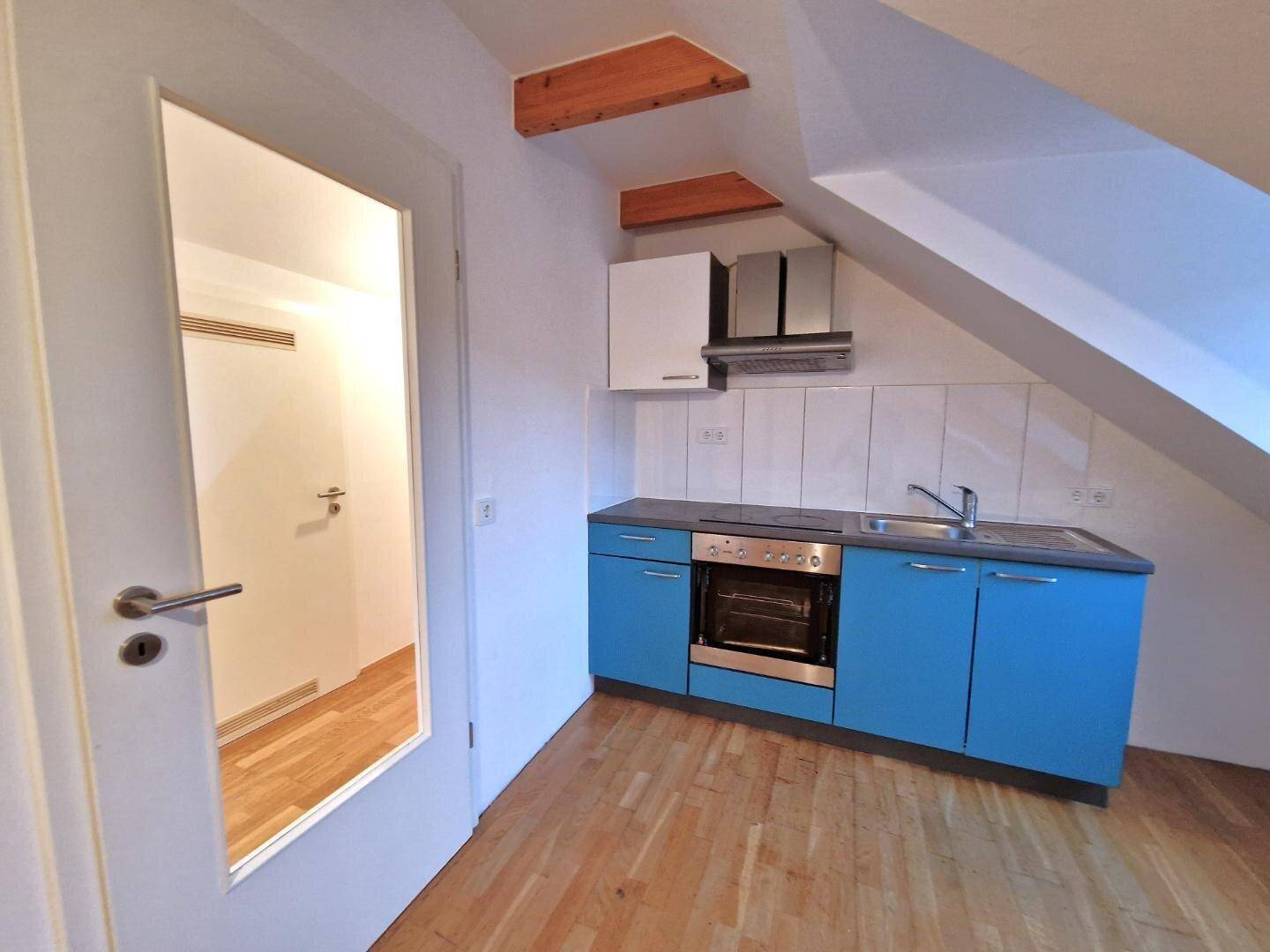 Funktionale Küchenzeile mit blauen Unterschränken, Herd und Spüle im Dachgeschoss.