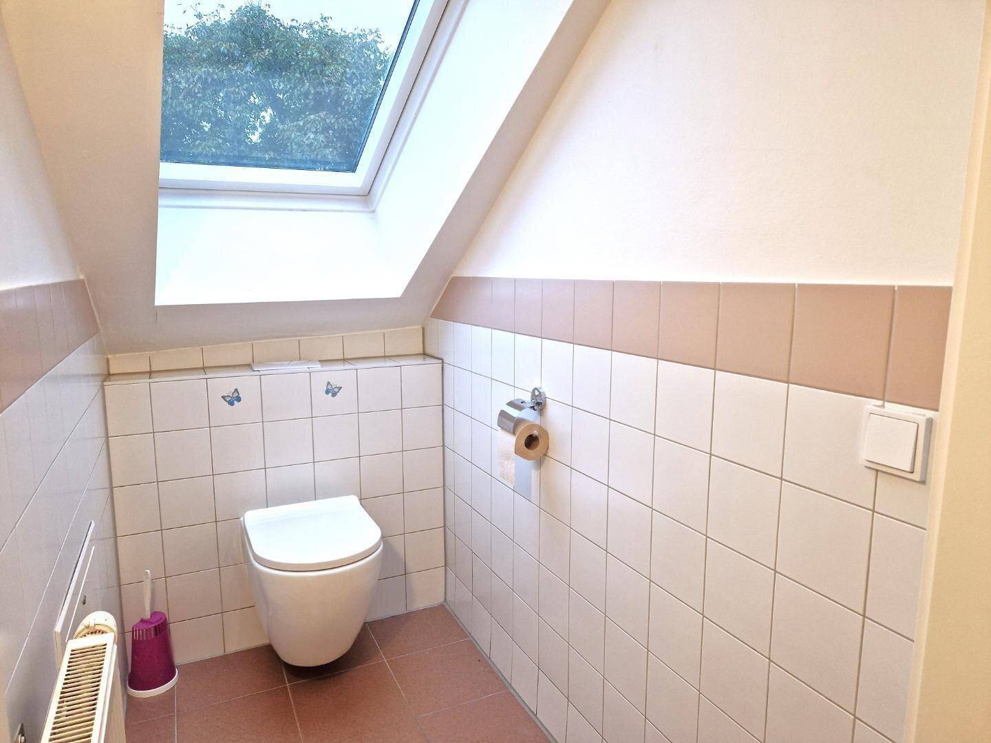 Separates WC mit wandhängender Toilette, Dachfenster und hellen Fliesen.