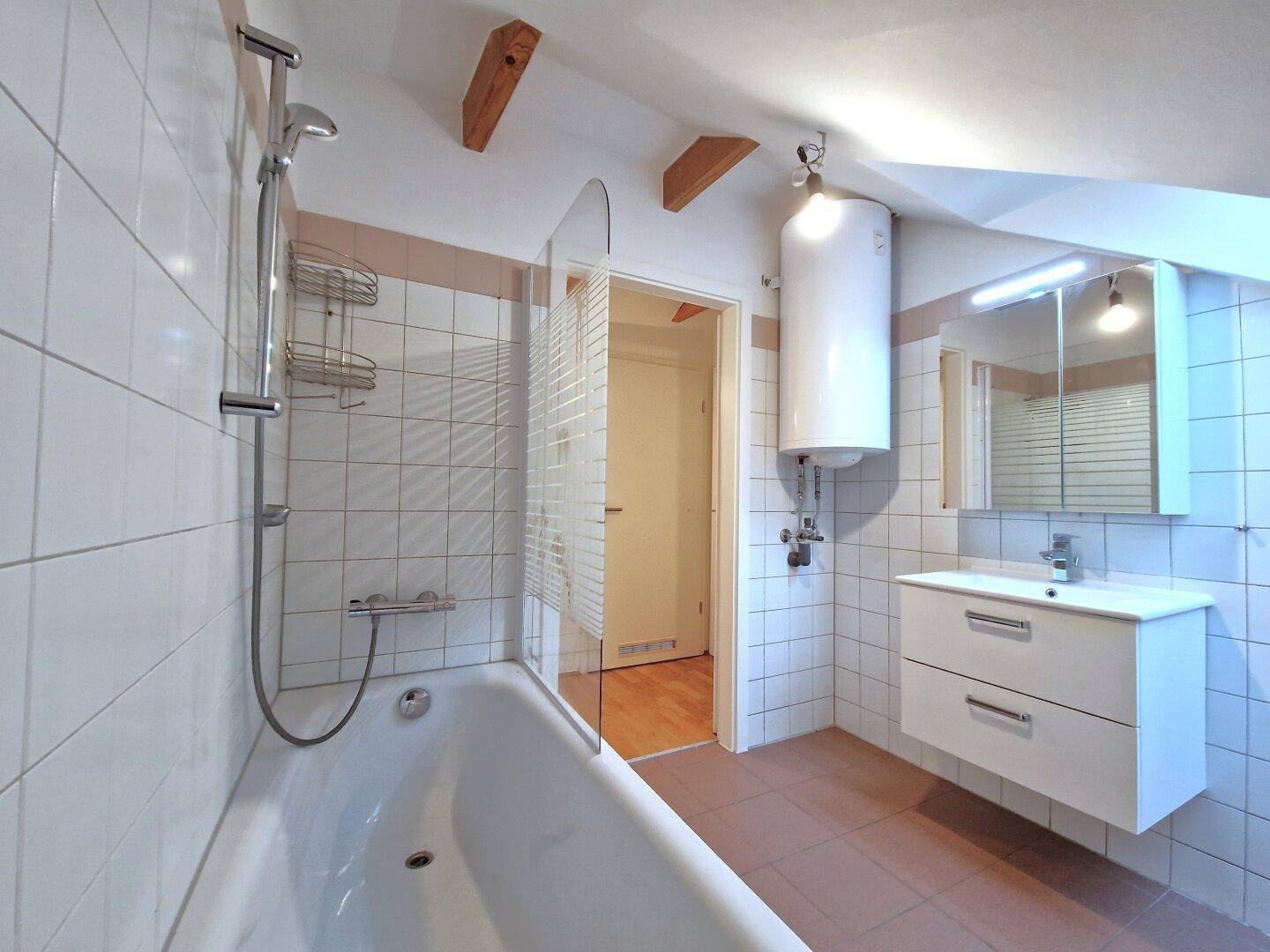 Badezimmer im Dachgeschoss mit Badewanne, Dusche, Waschbecken und praktischem Spiegelschrank.