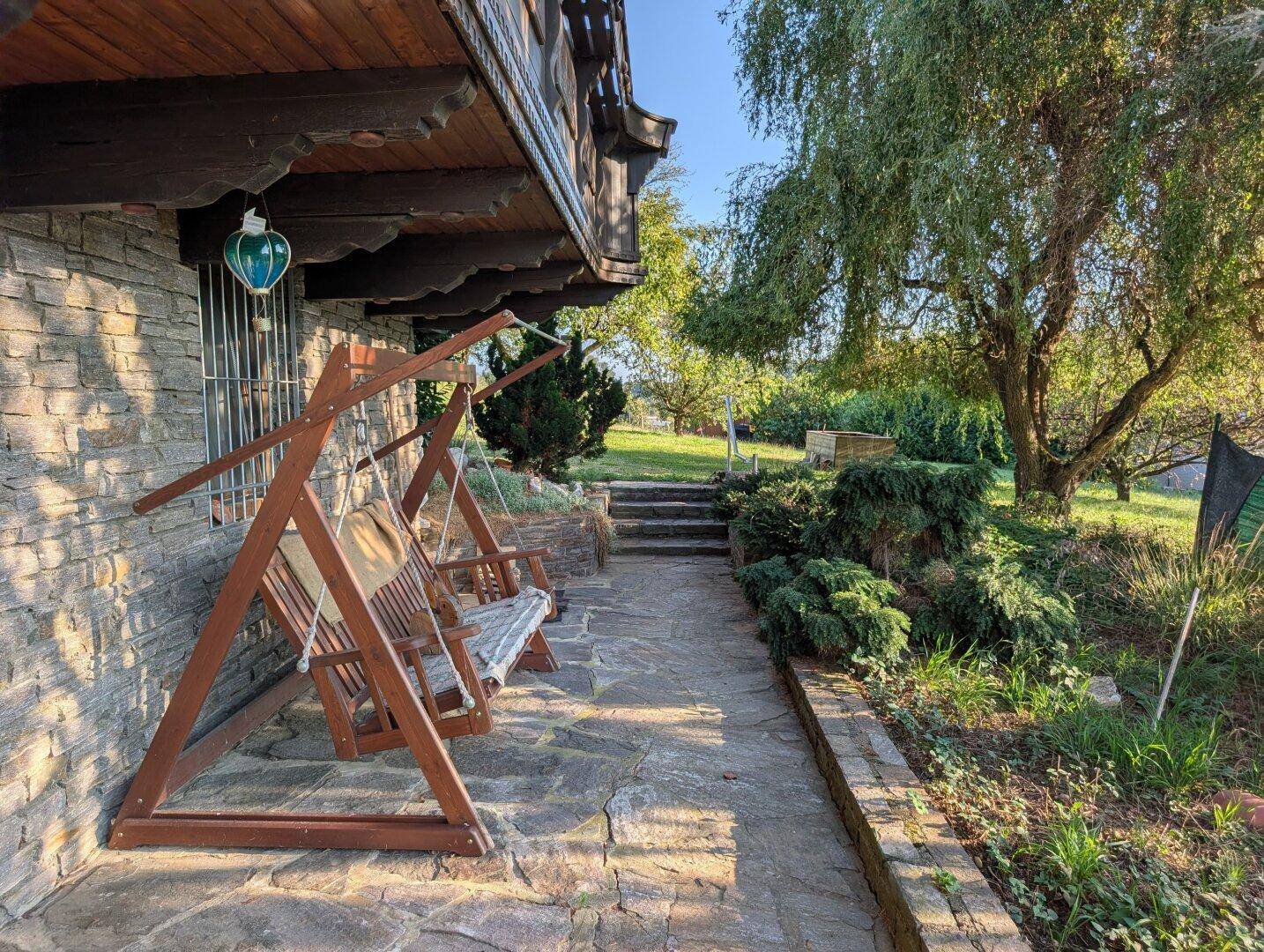 Gemütlicher Gartenbereich mit Steinterrasse, Holzschaukel und altem Baumbestand.