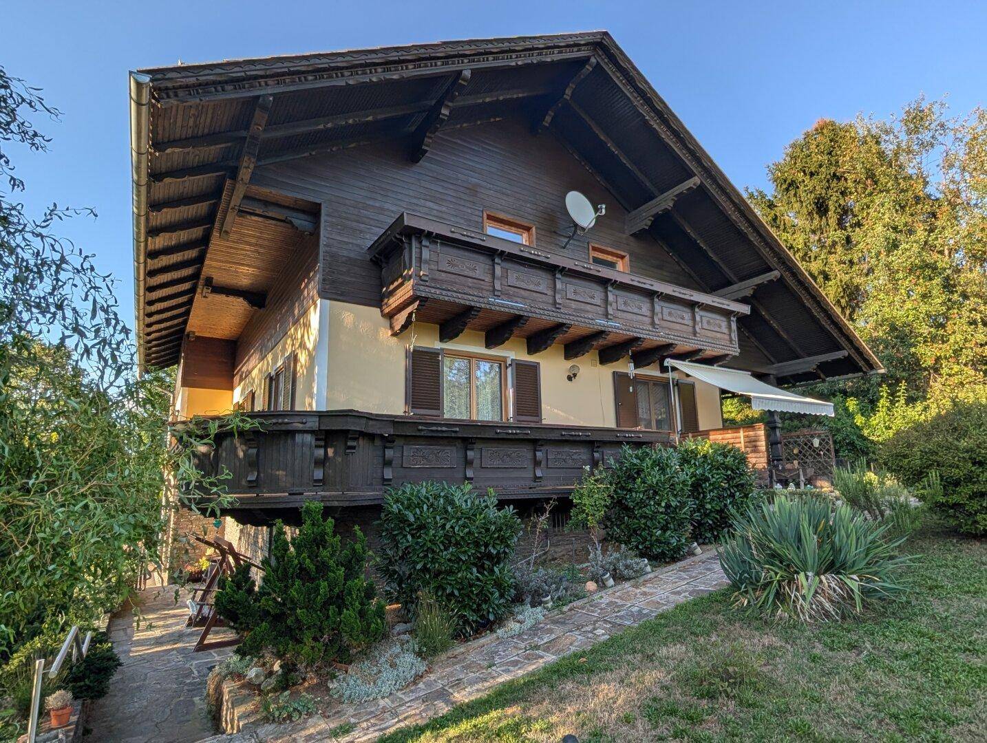 Seitenansicht des traditionellen Landhauses mit Holzbalkonen und gepflegtem Gartenbereich im Vordergrund.