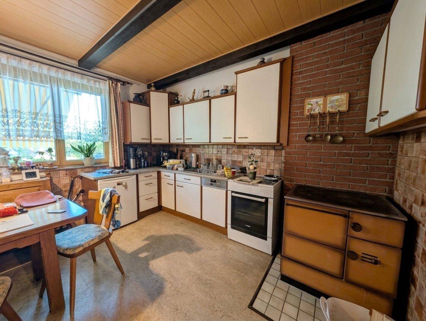 Rustikale Küche mit Holzdecke, Backsteinwand und einem traditionellen Holzofen neben modernen Schränken.