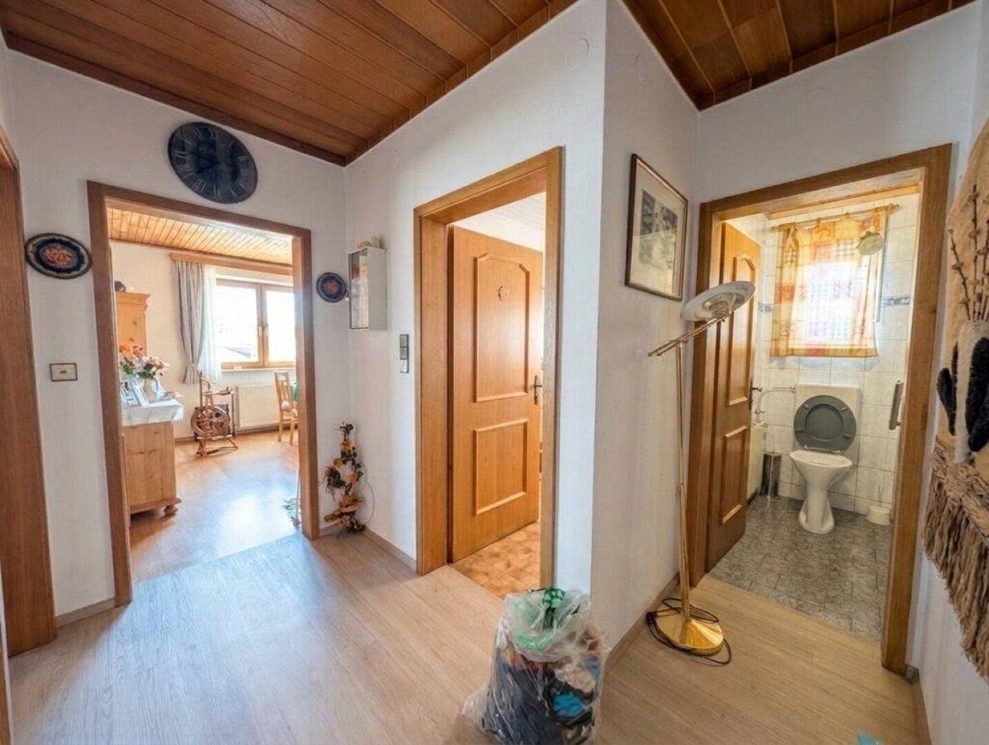 Flur mit Holzdecke und Zugang zu einem kleinen WC mit einfacher Ausstattung und Fliesenboden.