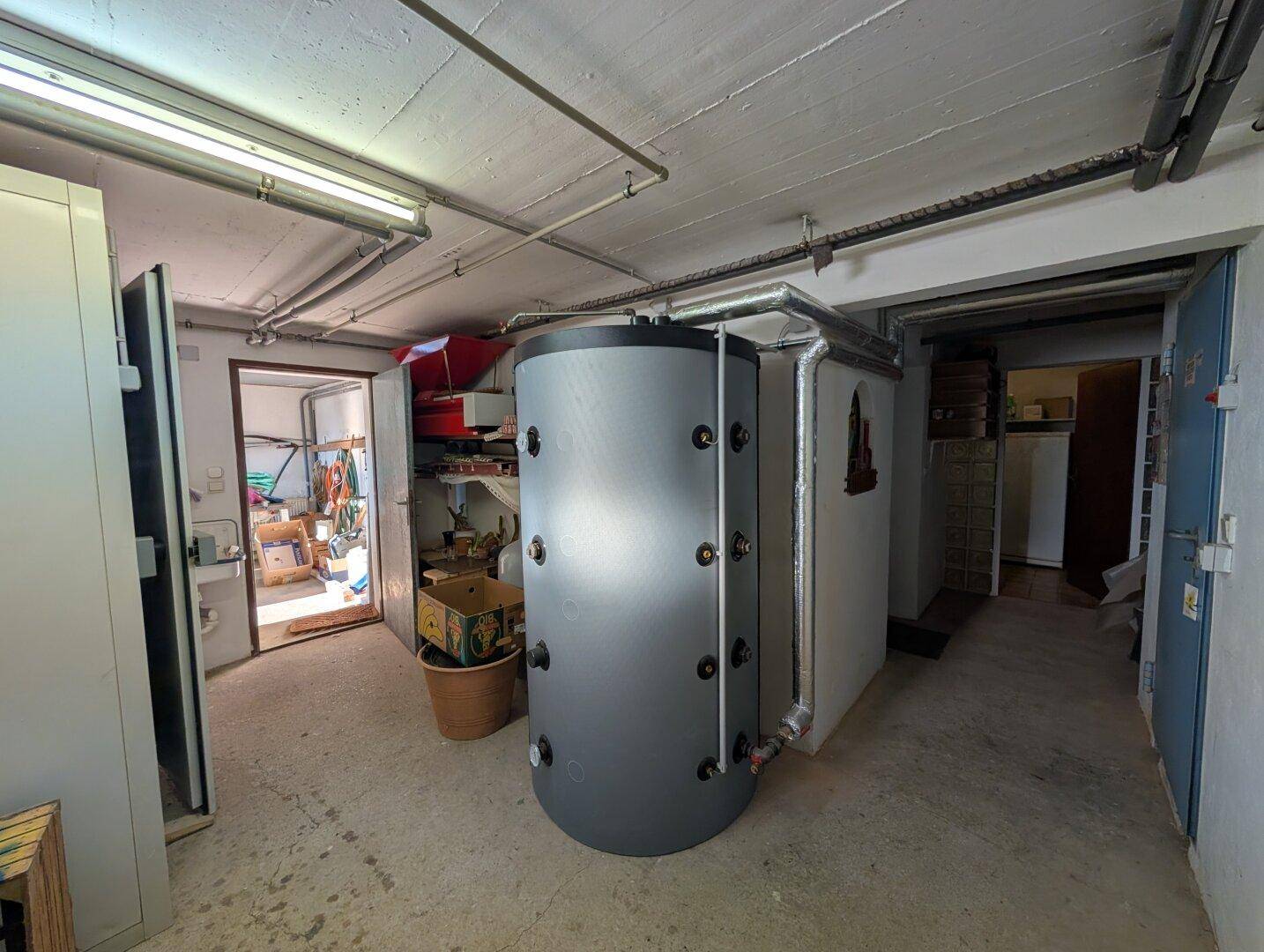 Technikraum im Keller mit großem Warmwasserspeicher und Zugang zu weiteren Räumen.