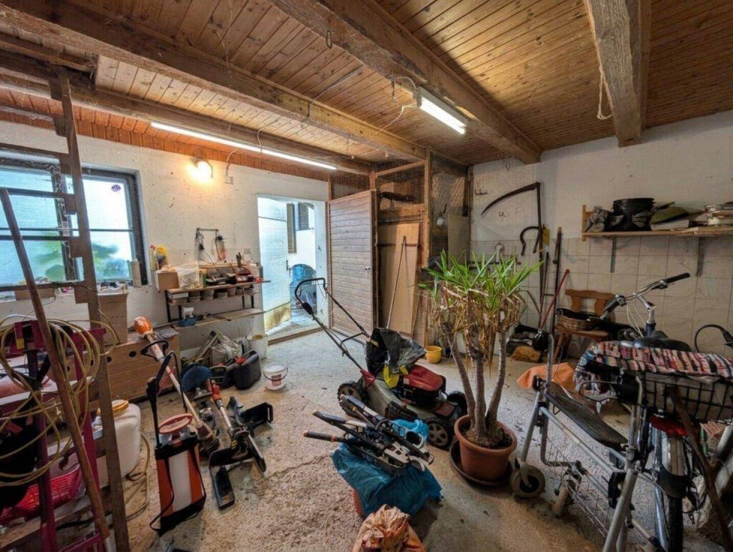 Unaufgeräumter Abstellraum mit Werkzeugen, Gartengeräten und sichtbaren Holzdeckenbalken.